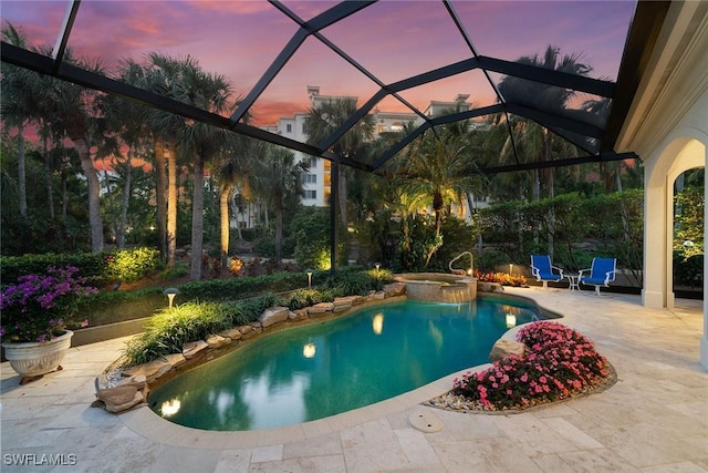 pool at dusk featuring glass enclosure, a patio area, and an in ground hot tub