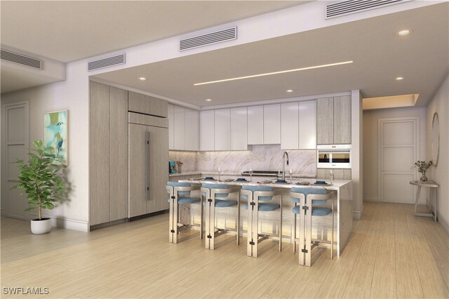 kitchen featuring paneled fridge, oven, white cabinetry, a breakfast bar area, and an island with sink