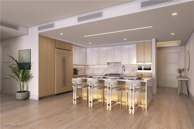 kitchen with white cabinetry, paneled fridge, a kitchen breakfast bar, oven, and a kitchen island with sink