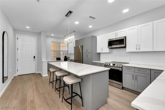 kitchen featuring gray cabinetry, backsplash, hanging light fixtures, a kitchen island, and stainless steel appliances