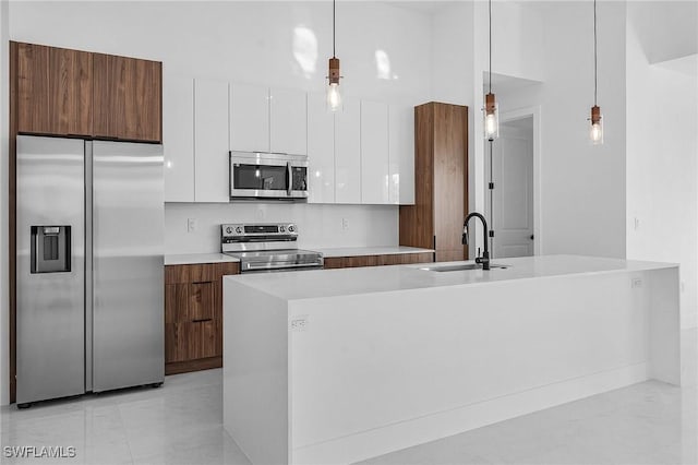 kitchen featuring a kitchen island with sink, sink, hanging light fixtures, white cabinetry, and stainless steel appliances