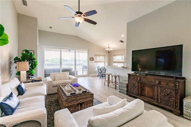 living room with vaulted ceiling, ceiling fan with notable chandelier, and light wood-type flooring