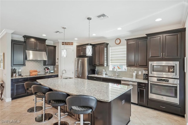 kitchen with hanging light fixtures, stainless steel appliances, a center island with sink, a kitchen bar, and sink