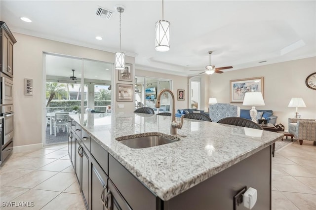 kitchen featuring a tray ceiling, light tile patterned floors, visible vents, open floor plan, and a sink