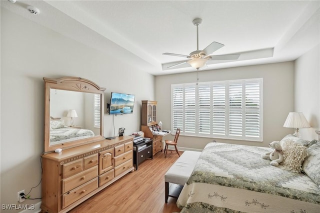 bedroom featuring light wood-type flooring, ceiling fan, and a tray ceiling