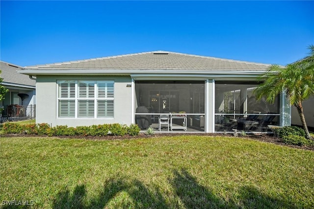 rear view of house featuring stucco siding, a tile roof, a sunroom, and a yard