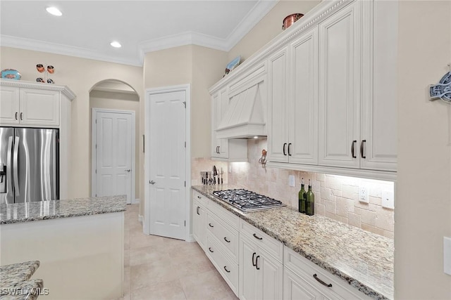 7440 Byrons Way, Naples, FL 34113 - kitchen featuring stainless steel appliances, light stone countertops, decorative backsplash, arched walkways, and white cabinets