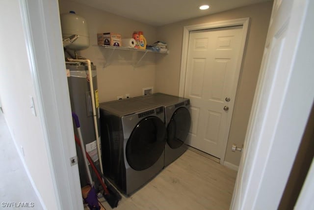 washroom with water heater, light hardwood / wood-style flooring, and washing machine and clothes dryer