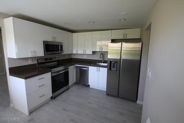 kitchen with appliances with stainless steel finishes, light wood-type flooring, white cabinetry, and sink