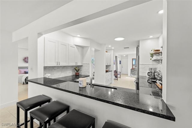 kitchen featuring dark stone counters, kitchen peninsula, white cabinets, and light tile patterned flooring