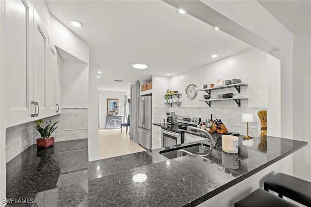 kitchen with appliances with stainless steel finishes, white cabinetry, sink, dark stone counters, and kitchen peninsula