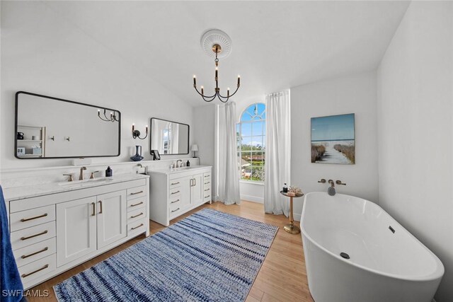 bathroom featuring vaulted ceiling, wood-type flooring, vanity, a notable chandelier, and a bath