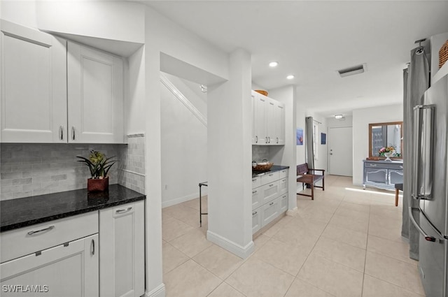 kitchen featuring tasteful backsplash, white cabinetry, dark stone countertops, and light tile patterned floors