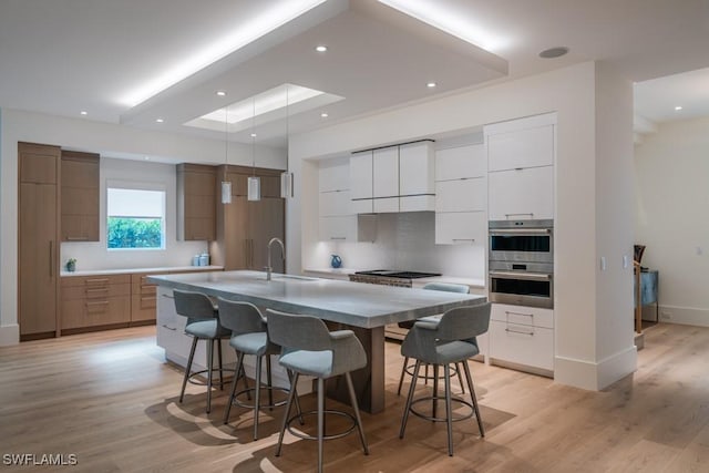 kitchen with a spacious island, a kitchen bar, sink, stainless steel appliances, and white cabinets