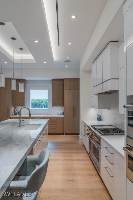 kitchen with sink, white cabinetry, hanging light fixtures, a tray ceiling, and light wood-type flooring