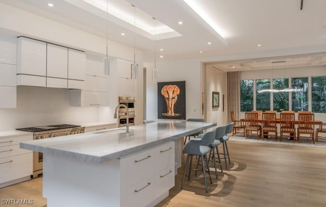 kitchen featuring high end stainless steel range oven, decorative light fixtures, a center island with sink, and white cabinets