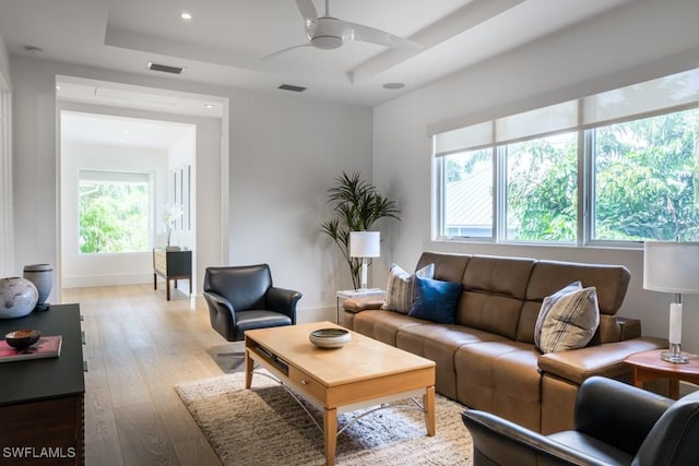 living room featuring ceiling fan, a tray ceiling, and light hardwood / wood-style floors