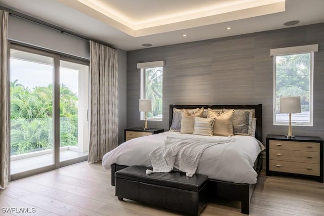 bedroom featuring access to exterior, a tray ceiling, and light hardwood / wood-style floors