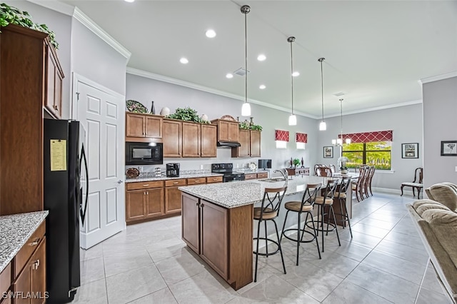 kitchen with light stone countertops, decorative light fixtures, a breakfast bar, black appliances, and a center island with sink