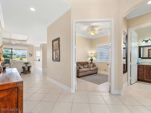 hallway featuring a raised ceiling, ornamental molding, and light tile patterned floors