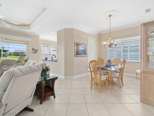 dining space with a raised ceiling, light tile patterned floors, ceiling fan with notable chandelier, and ornamental molding