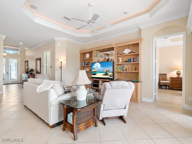 tiled living room with a tray ceiling, crown molding, and ceiling fan