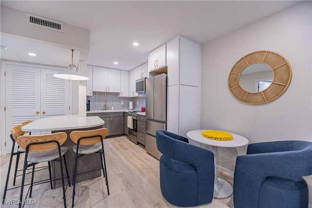 kitchen with pendant lighting, backsplash, light hardwood / wood-style flooring, white cabinetry, and stainless steel appliances