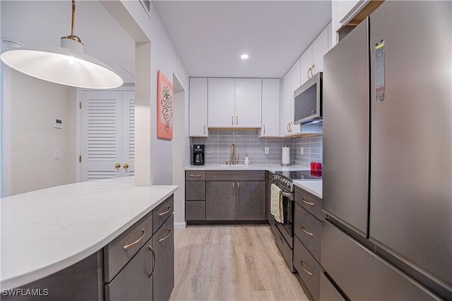 kitchen featuring appliances with stainless steel finishes, backsplash, sink, white cabinetry, and hanging light fixtures