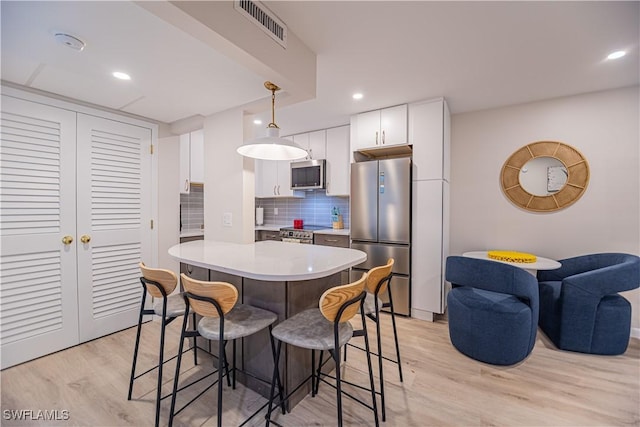 kitchen with appliances with stainless steel finishes, light wood-type flooring, tasteful backsplash, pendant lighting, and white cabinetry