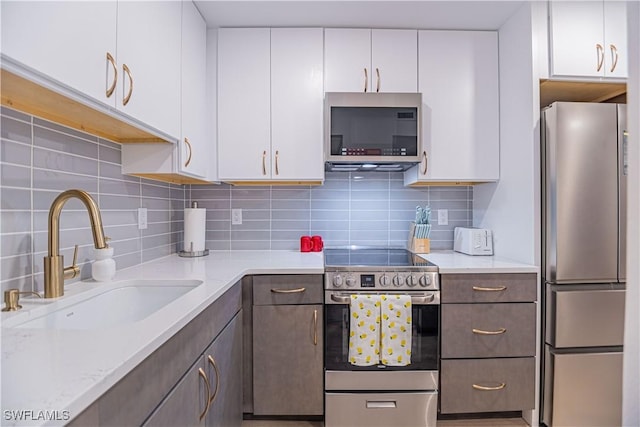 kitchen featuring sink, stainless steel appliances, tasteful backsplash, light stone counters, and white cabinets