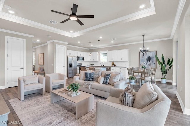 living room with ceiling fan with notable chandelier, crown molding, light hardwood / wood-style floors, and sink