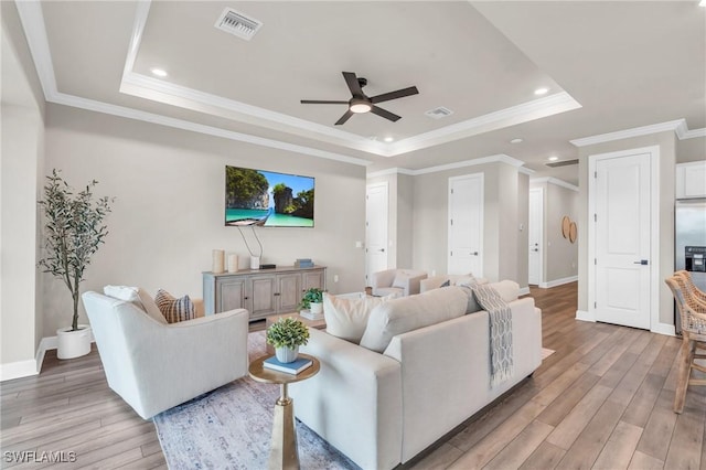 living room featuring ceiling fan, ornamental molding, light hardwood / wood-style floors, and a tray ceiling