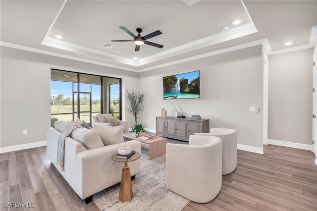 living room with light wood-type flooring, ceiling fan, and a tray ceiling