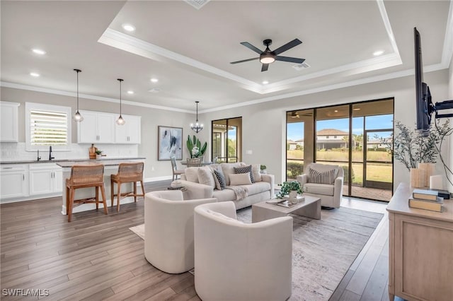 living room with light wood-type flooring, a tray ceiling, and ceiling fan with notable chandelier