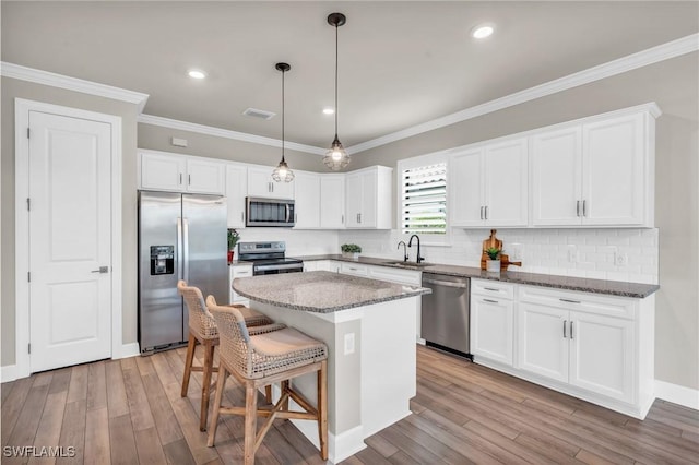 kitchen with appliances with stainless steel finishes, white cabinetry, dark stone counters, and a center island