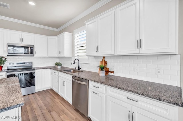 kitchen featuring white cabinetry, stainless steel appliances, decorative backsplash, dark stone counters, and sink