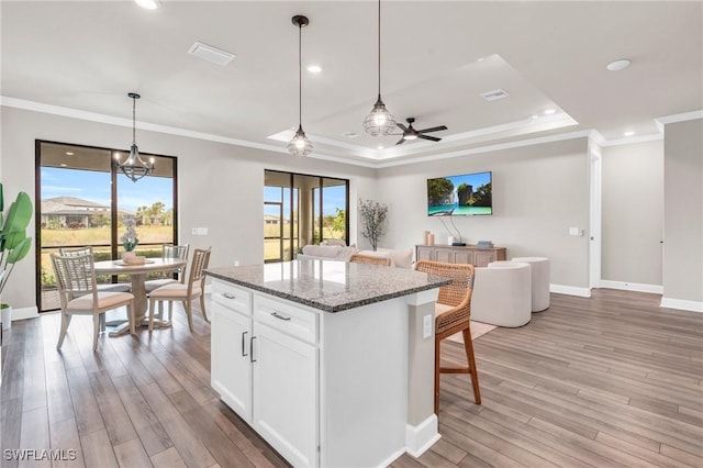 kitchen featuring white cabinetry, hanging light fixtures, stone counters, ceiling fan with notable chandelier, and a center island