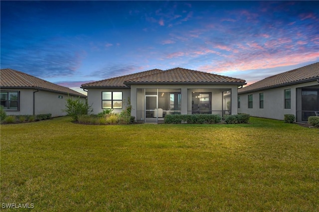 back house at dusk with a lawn and a sunroom