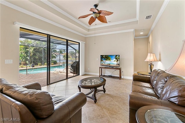 living room featuring ceiling fan, light tile patterned flooring, a tray ceiling, and ornamental molding