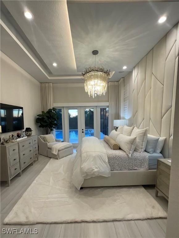 bedroom featuring an inviting chandelier, french doors, light hardwood / wood-style flooring, access to exterior, and a tray ceiling