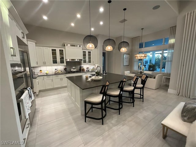 kitchen with backsplash, a kitchen island with sink, white cabinetry, hanging light fixtures, and a breakfast bar area