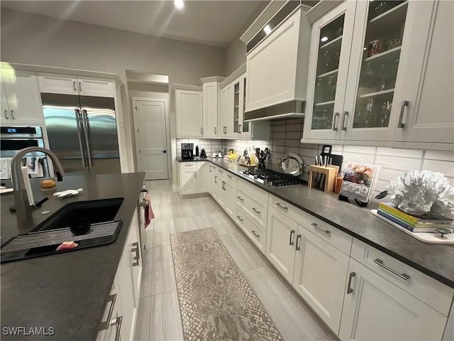 kitchen with white cabinetry, sink, stainless steel appliances, decorative backsplash, and custom range hood