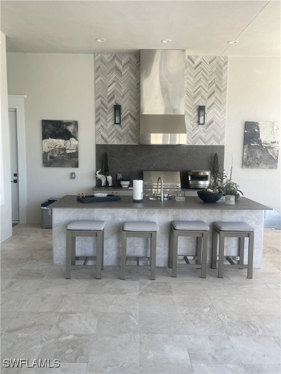 kitchen with a breakfast bar, wall chimney range hood, and sink