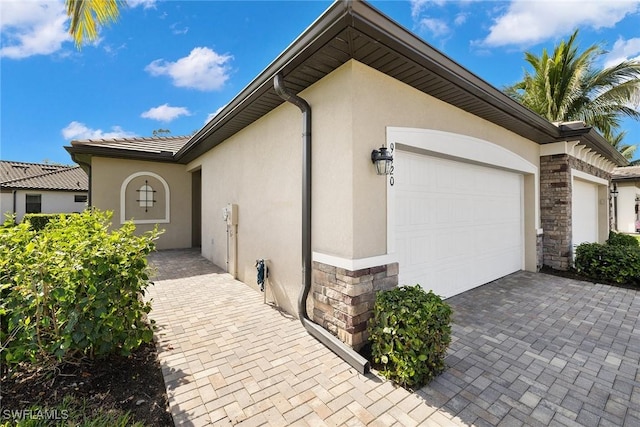 view of property exterior featuring a garage, stone siding, decorative driveway, and stucco siding