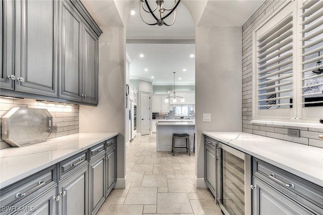 kitchen featuring wine cooler, gray cabinets, pendant lighting, and a notable chandelier