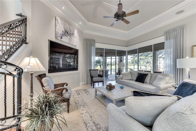 living room with a raised ceiling, ceiling fan, and ornamental molding