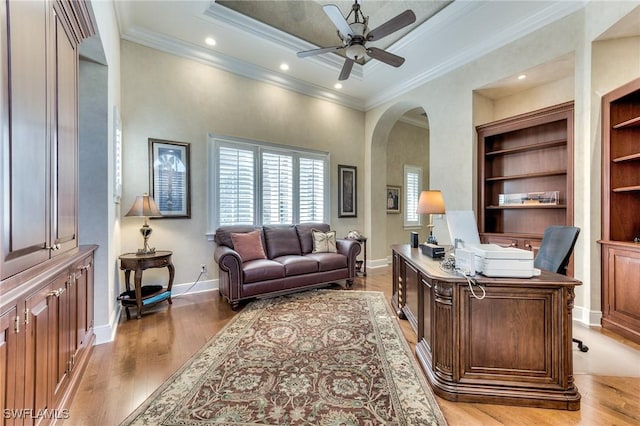 office area with ceiling fan, a raised ceiling, built in features, crown molding, and light wood-type flooring