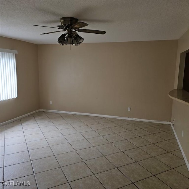 empty room with ceiling fan, light tile patterned floors, and a textured ceiling