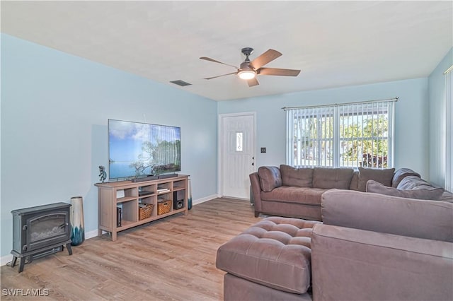 living room with light wood-type flooring, a wood stove, and ceiling fan