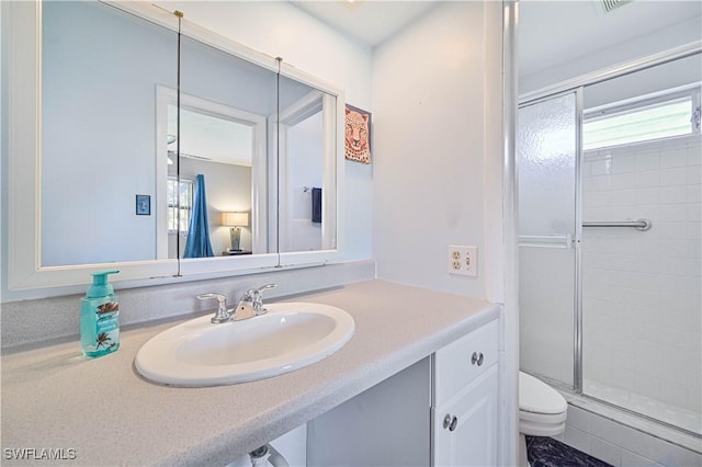 bathroom featuring vanity, a healthy amount of sunlight, toilet, and a shower with shower door